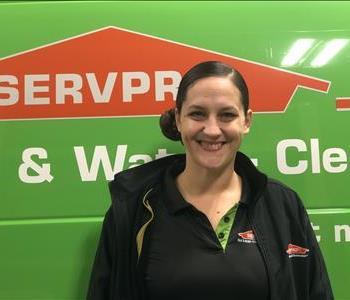 Female employee with brown hair standing in front of a green Servpro vehicle
