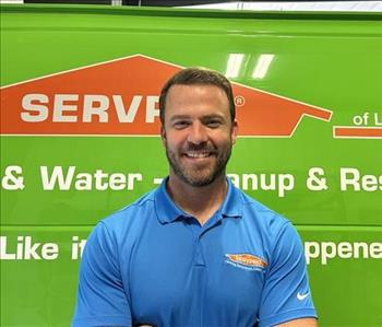 Smiling man in a blue shirt with light brown hair and a light beard, standing in front of a green Servpro work van. 