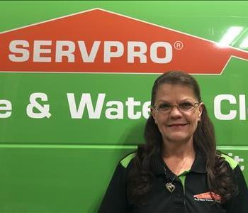 Female employee with brown hair standing in front of a green Servpro vehicle