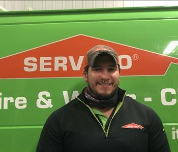 Male employee wearing a baseball cap standing in front of a green Servpro vehicle