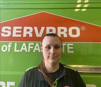 Young woman with blonde hair in a pony tail, standing in front of a green Servpro work vehicle. 