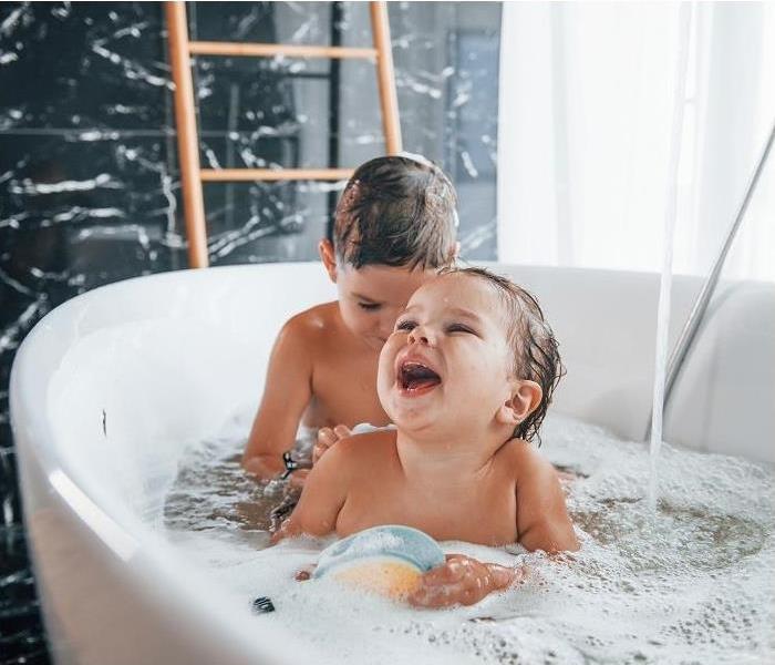 Two toddlers playing in bathtub; lots of suds, water