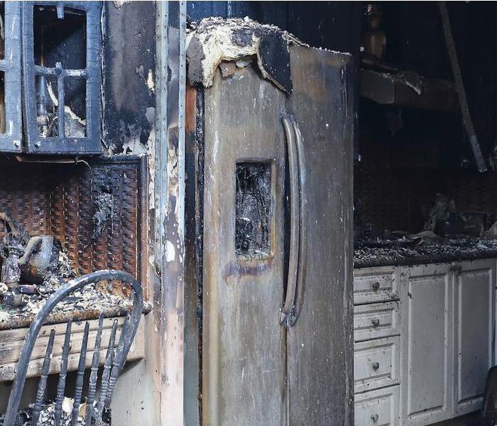 residential kitchen with burned fridge and cabinets. Soot covering the counters and walls