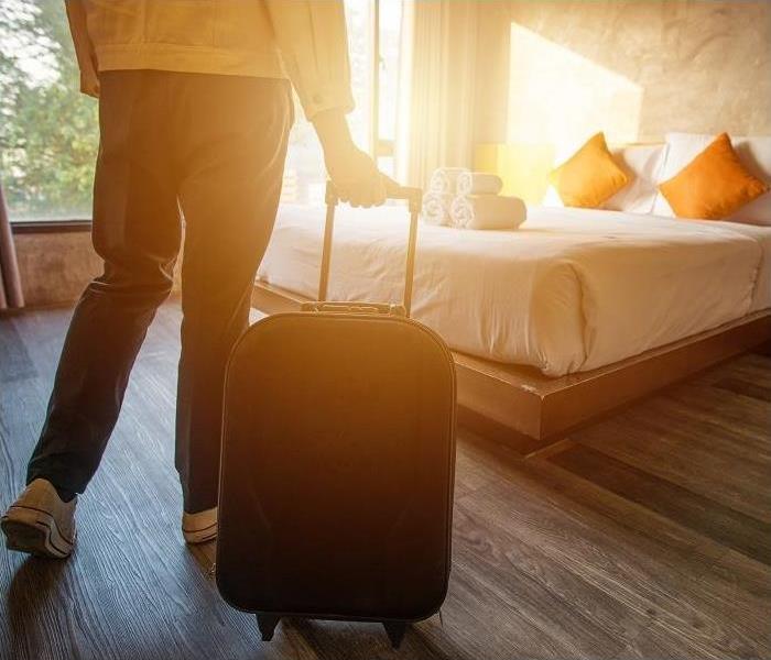Person with suitcase entering sunny hotel room 